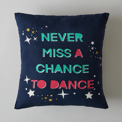 Decorative square cushion with multicoloured "Never Miss a Chance to Dance" text design.